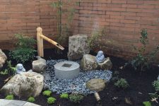 a small Japanese front yard with pebbles, greenery, a stone and bamboo fountain, rocks, shrubs is a lovely space