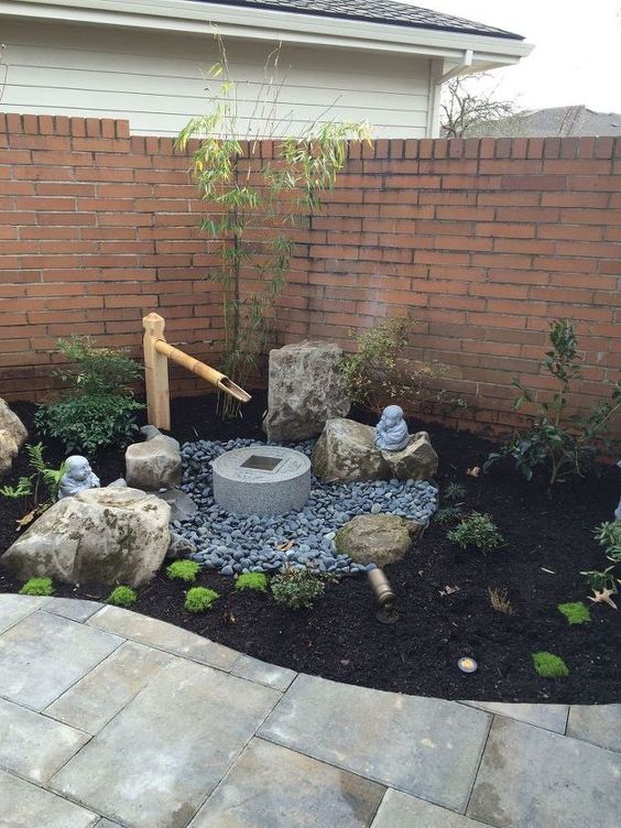 un pequeño patio delantero japonés con guijarros, vegetación, una fuente de piedra y bambú, rocas y arbustos es un espacio encantador