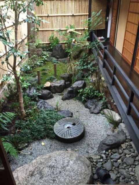a small Japanese space with a stone bowl, greenery and moss, a bamboo fountain, a low tree and rocks