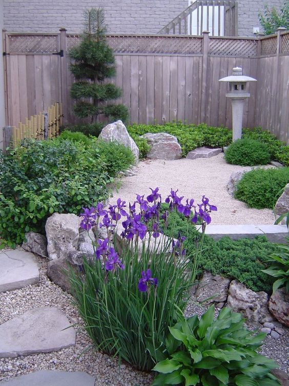 a small Japanese space with greenery and rocks, a tree and a traditional stone lantern that can be on at night