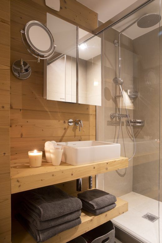 a small and lovely chalet bathroom done with blonde wood, with an open vanity, a shower space done with concrete and a couple of mirrors