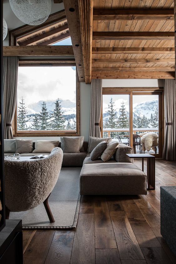 a soothing contemporary chalet with large windows, a low grey sofa, a neutral chair and some tables is wow