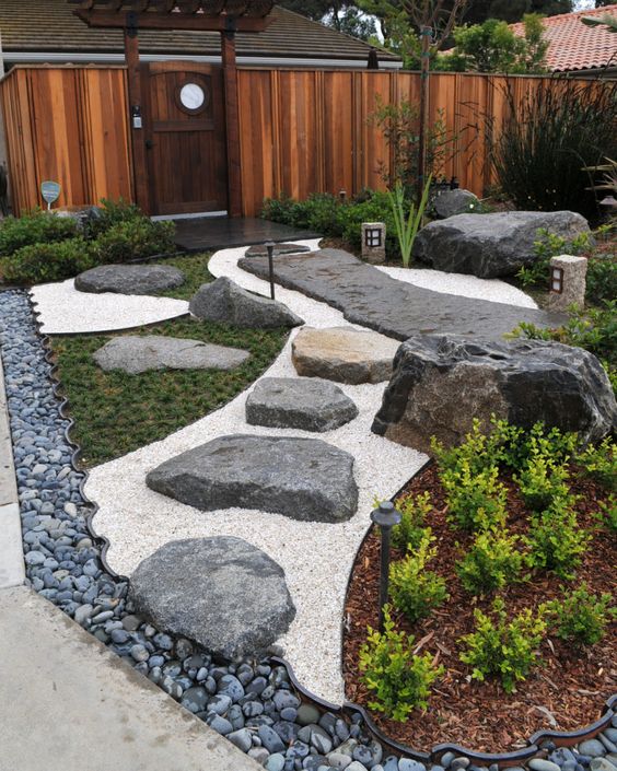 un elegante patio delantero japonés con guijarros, rocas, vegetación, un camino de rocas y linternas es una hermosa idea de decoración moderna