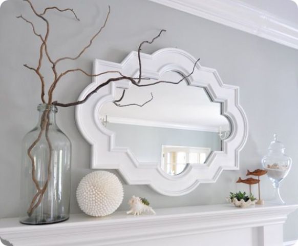 a summer coastal mantel with seashells, greenery, fish figurines, branches and a vintage mirror