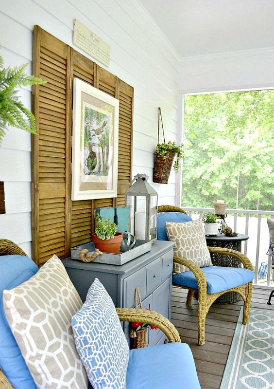a summer porch with rattan chairs, printed pillows, a grey dresser and shutter decor