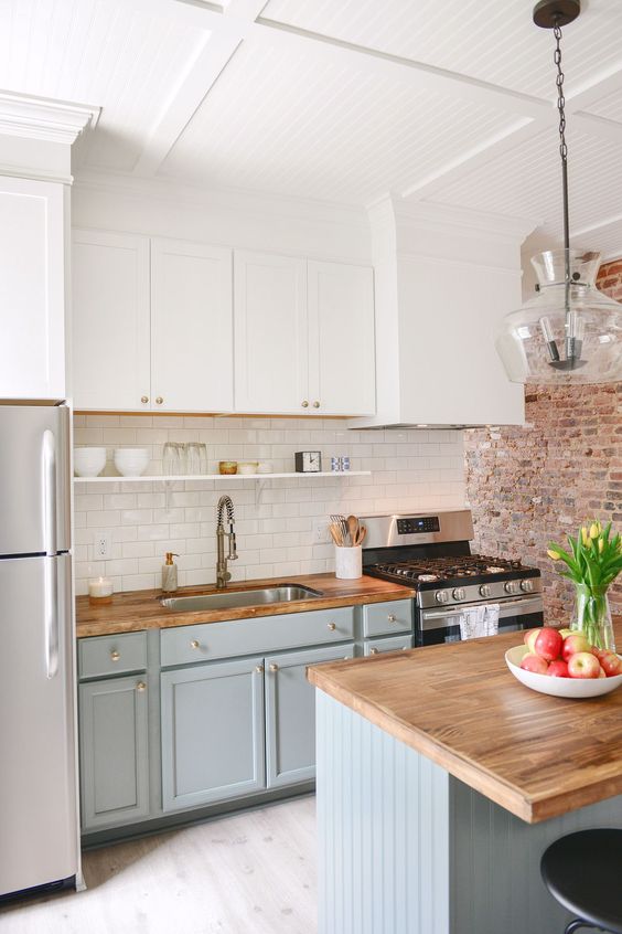 a two tone kitchen with white and dove grey cabinets, light stained butcherblock countertops and gold touches