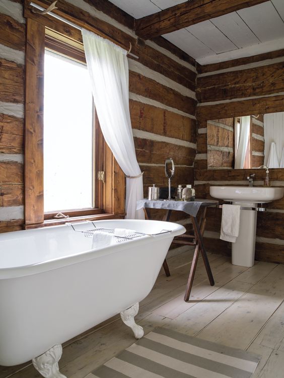 a vintage chalet bathroom with various types of wood, a clawfoot tub, a free-standing sink and a trestle table, neutral textiles