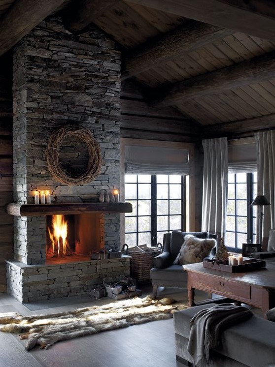 a vintage chalet living room with wooden walls and a ceiling, a stone fireplace and faux fur accessories