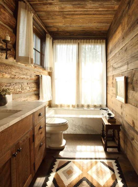 a vintage-inspired chalet bathroom completely clad with wood, with a wooden vanity, a printed rug, a bathtub clad with marble and vintage furniture