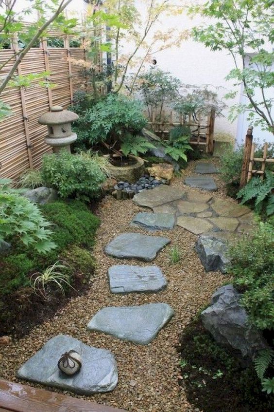 un acogedor patio japonés con rocas, vegetación, musgo, un farol de piedra y una fuente de bambú, además de una cerca baja