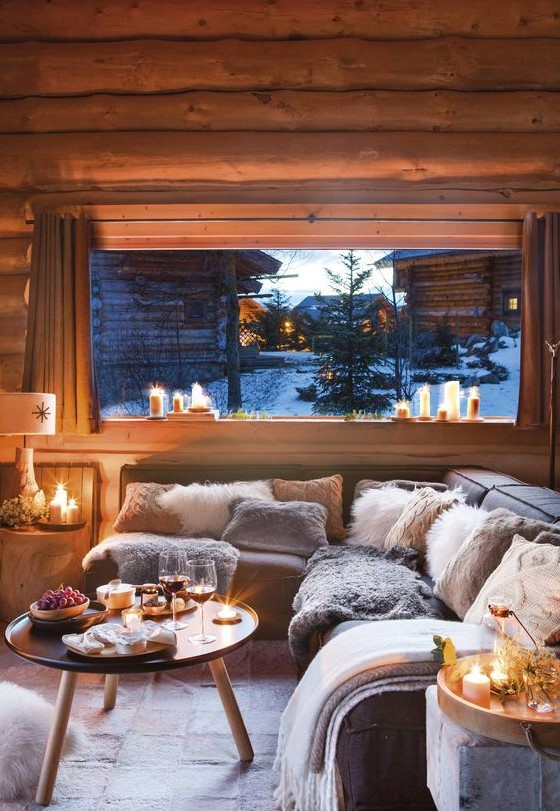 a welcoming chalet living room all clad with wood, comfy furniture, a round table and lots of candles