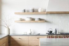 an airy minimalist kitchen with rough wooden cabinets, concrete countertops, a white tile backsplash and a white hood