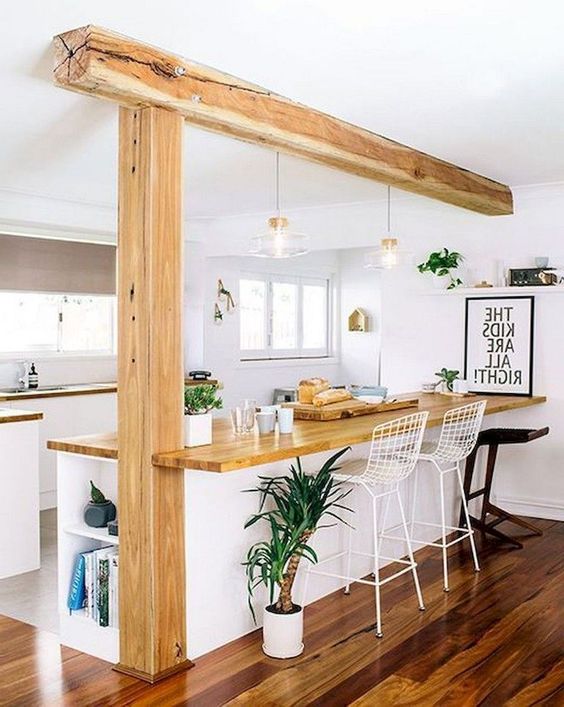 an airy modern white kitchen with light stained butcherblock countertops that match the wooden beam and pillar