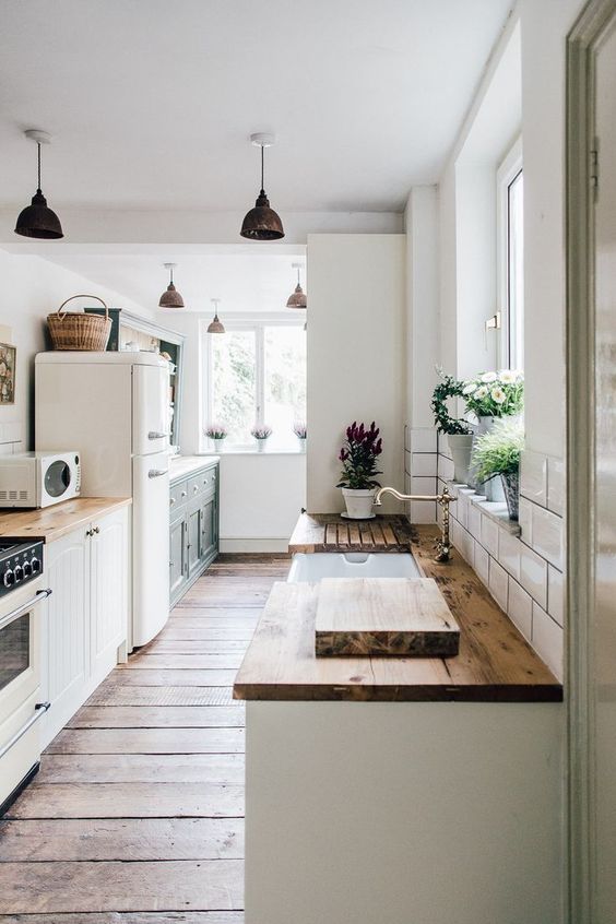 an airy white kitchen with rich stained wooden countertops and brass and darkened metal touches for a more vintage feel