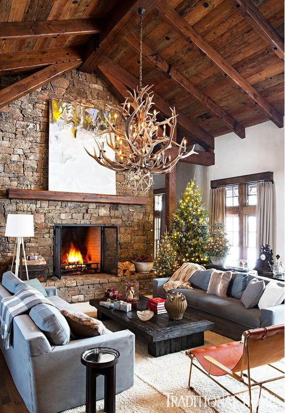 an inviting chalet living room with a wooden ceiling with beams, a stone fireplace, an antler chandelier and chic and cool furniture