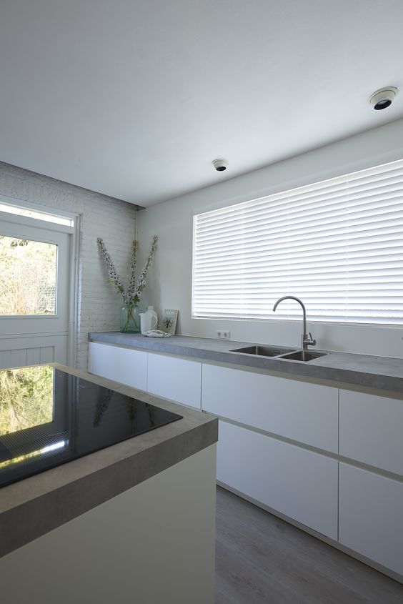 an ultra-minimalist kitchen in white, with sleek cabinets, concrete countertops and a kitchen island with built-ins