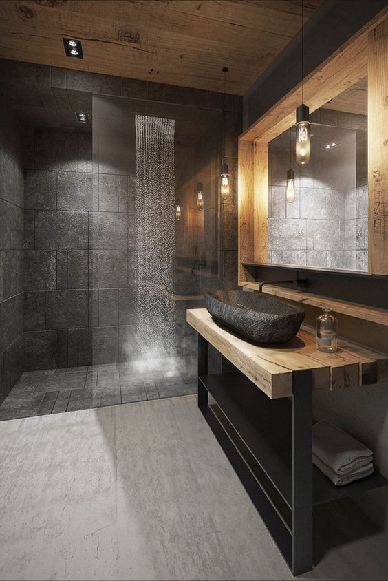 an ultra-modern chalet bathroom done with black stone tiles, a bit of blonde wood, blackened metal and a stone sink