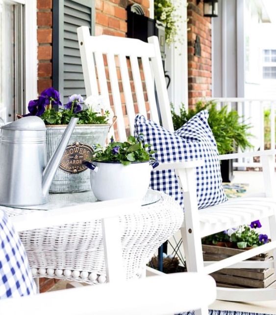 farmhouse porch decor with white wooden and wicker furniture, gingham textiles, potted blooms and greenery