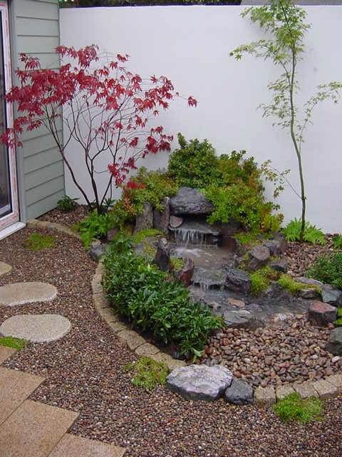 pebbles, tiles, a waterfall on rocks, shrubs and mini thin trees will make your outdoor space super inspiring and calming