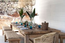 a Mediterranean dining spot with a roof with pendant lamps, stained dinign set with benches, a wicker chair and blue glasses