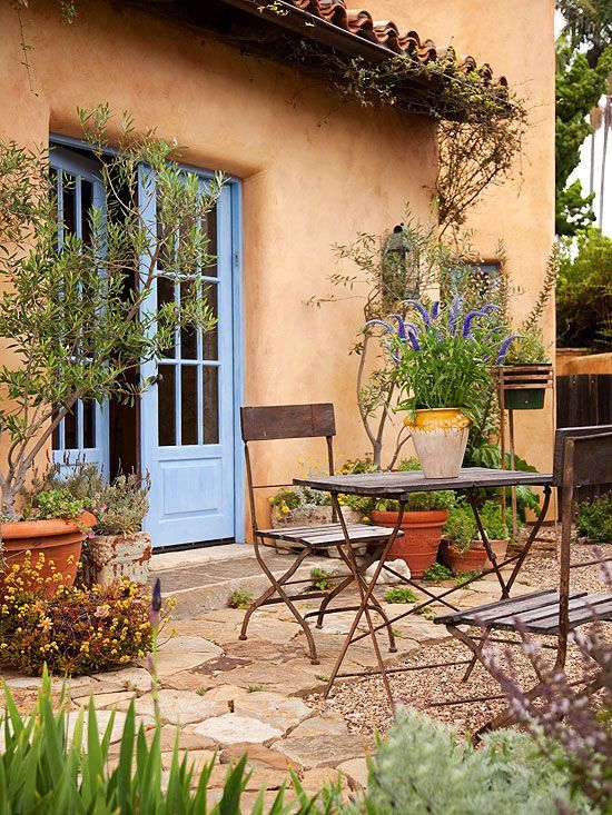 a Mediterranean outdoor dining space with shabby chic plants with greenery and blooms, a folding table and chairs, candle lanterns