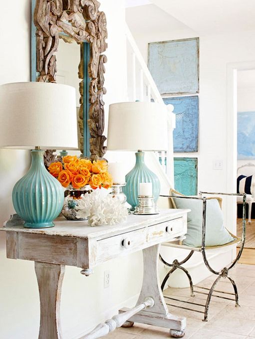 a beachy console table with aqua lamps, orange roses, corals and a mirror clad with driftwood is a cool idea for a coastal home