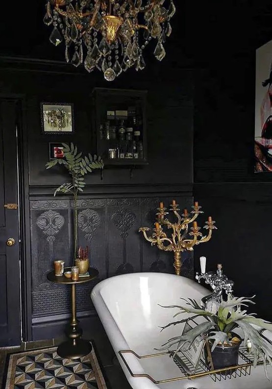 a beautiful black Gothic bathroom with black walls and black wallpaper, a black cabinet, a vintage bathtub, a crystal chandelier and candles