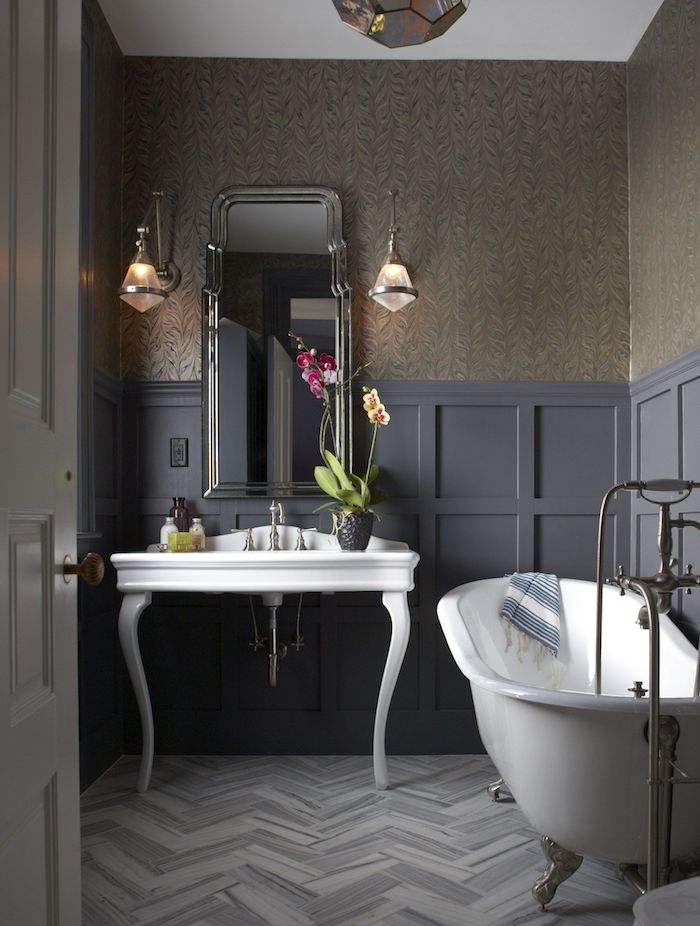 a chic moody bathroom with a vintage feel, a white free-standing sink and a bathtub, a mirror, sconces and blooms
