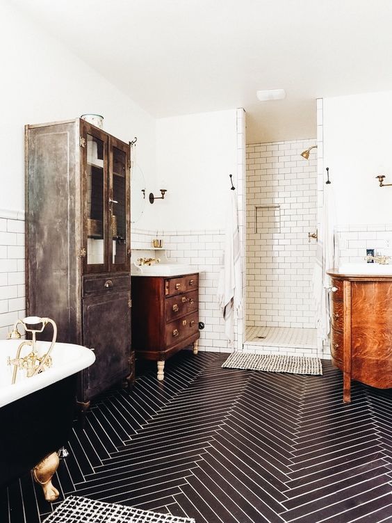 a chic vintage bathroom with a navy chevron tile floor, stained furniture, a black clawfoot bathtub, a white subway tile shower space