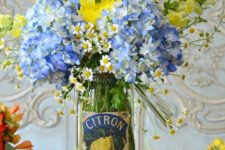 a clear jar with bright yellow and blue flowers is a bold and cool summer centerpiece with a vintage feel