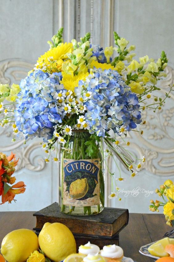 a clear jar with bright yellow and blue flowers is a bold and cool summer centerpiece with a vintage feel