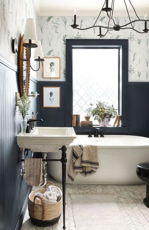 a contrasting bathroom with black paneled and floral print walls, a free-standing bathtub and sink, a chandelier and artwork is pure elegance