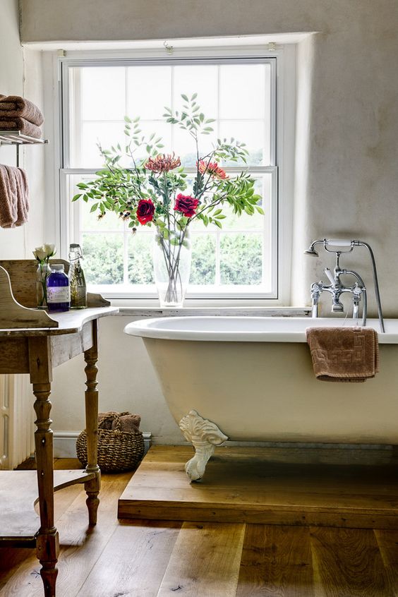 a country bathroom with neutral walls, a neutral clawfoot bathtub, a wooden vanity and blooms and towels