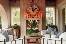 a cozy Mediterranean living room, outdoors and indoors, with a non-working fireplace, a round wooden table, metal chairs with white upholstery and greenery