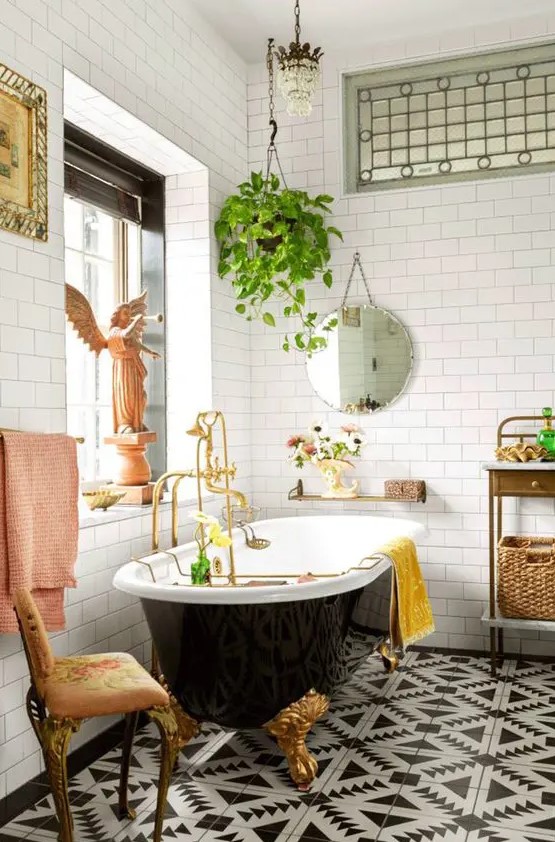 a fancy and whimsy bathroom with a gorgeous printed tile floor, a black vintage tub, a crystal chandelier and vintage furniture and a potted plant