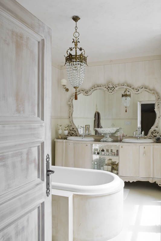 a jaw-dropping vintage bathroom in neutrals, with a double vanity, a mirror in an ornated frame, a bathtub and a crystal chandelier