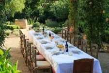 a large Mediterranean dining space with lots of greenery and trees, a long dining table, vintage chairs and chic table styling