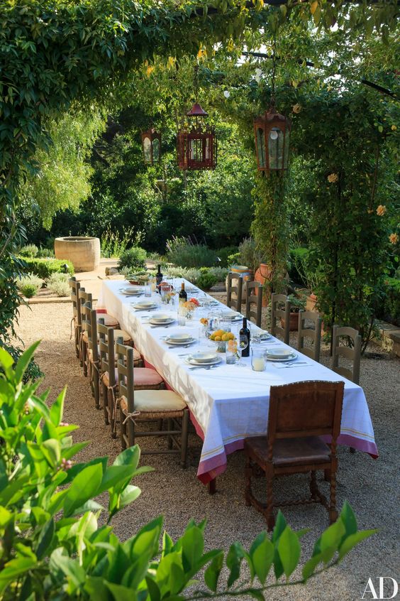 a large Mediterranean dining space with lots of greenery and trees, a long dining table, vintage chairs and chic table styling