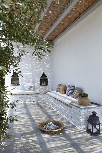 a lovely Mediterranean patio with a built-in bench and striped pillows, Moroccan lanterns, a tray with a magazine and greenery around