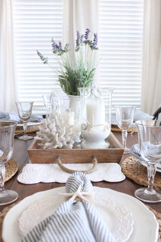 a lovely coastal farmhouse wedding centerpiece of a wooden tray, corals, candles in glasses with sand and some lavender is cool