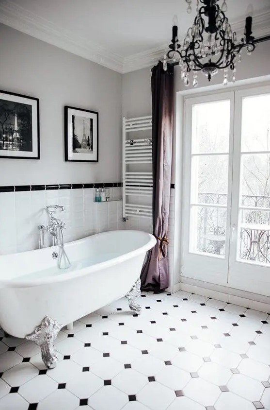 a lovely fancy bathroom with a black and white mosaic tile floor and tiles on the wall, a chic bathtub, purple curtains, a crystal chandelier