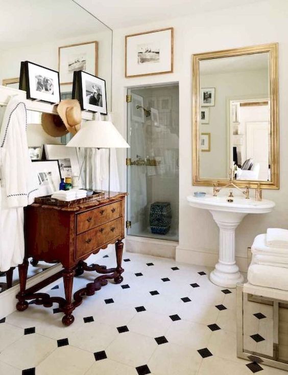 a neutral bathroom with black and white tile floor, a vintage dresser, a free-standing sink, a gallery wall and a couple of mirrors