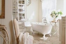a neutral cottage bathroom with paneling, a crystal chandelier, a neutral chair, a glass cabinet, floral and neutral textiles