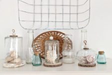 a pretty beach display with seashells and corals in jars and cloches plus blue bottles and a wicker basket