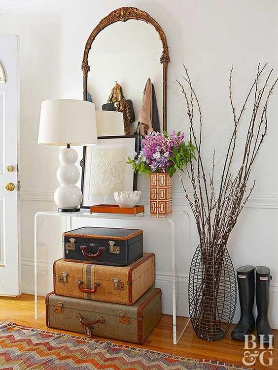 a pretty entryway with an acrylic console table, stacked suitcases, table lamps and blooms and some drawings is a cool space with a personality