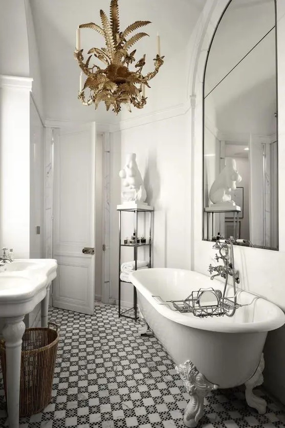 a refined and luxurious bathroom with white walls, a mosaic tile floor, a white vintage tub and an oversized mirror and a gold chandelier