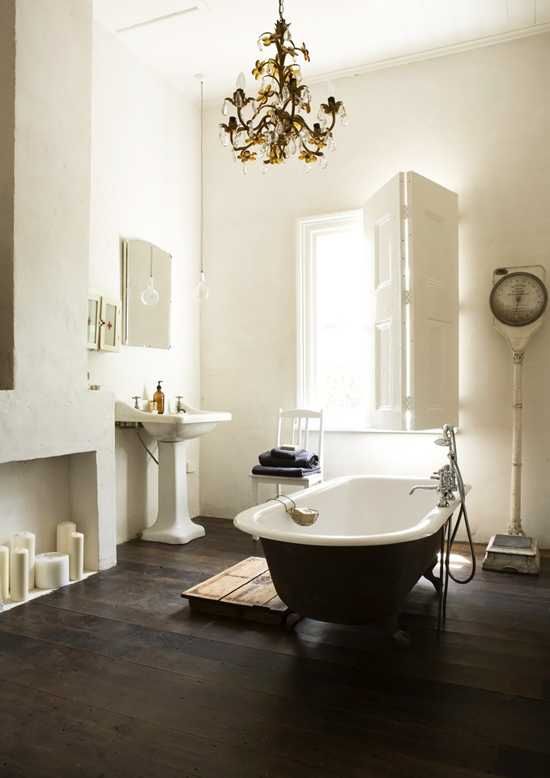 a refined vintage bathroom with a faux fireplace, a black clawfoot bathtub, a free-standing sink, a vintage chandelier and shutters on the window