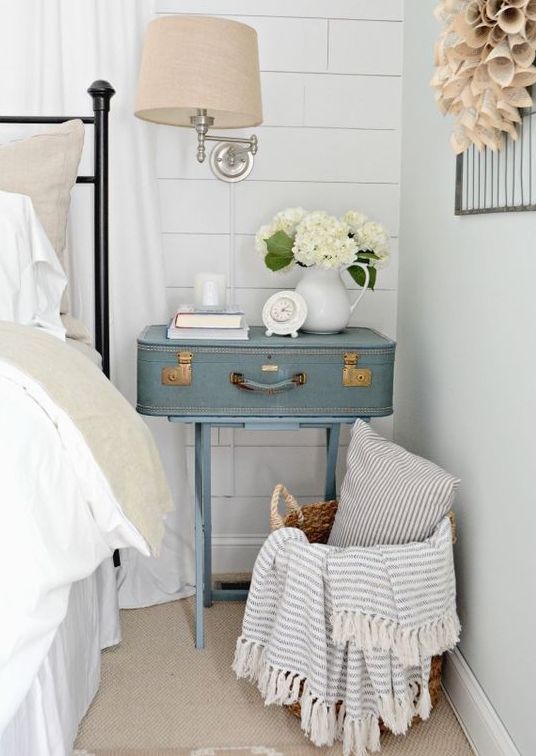 a serenity blue nightstand of a vintage suitcase on trestle legs, with a pastel sconce and some blooms