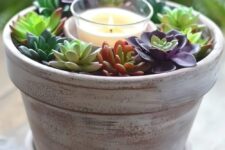 a simple decoration or centerpiece of a whitewashed planter with succulents and a candle in the center