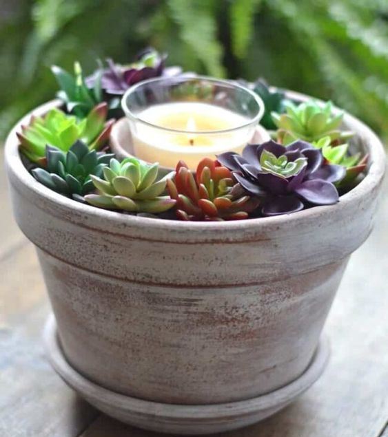 a simple decoration or centerpiece of a whitewashed planter with succulents and a candle in the center